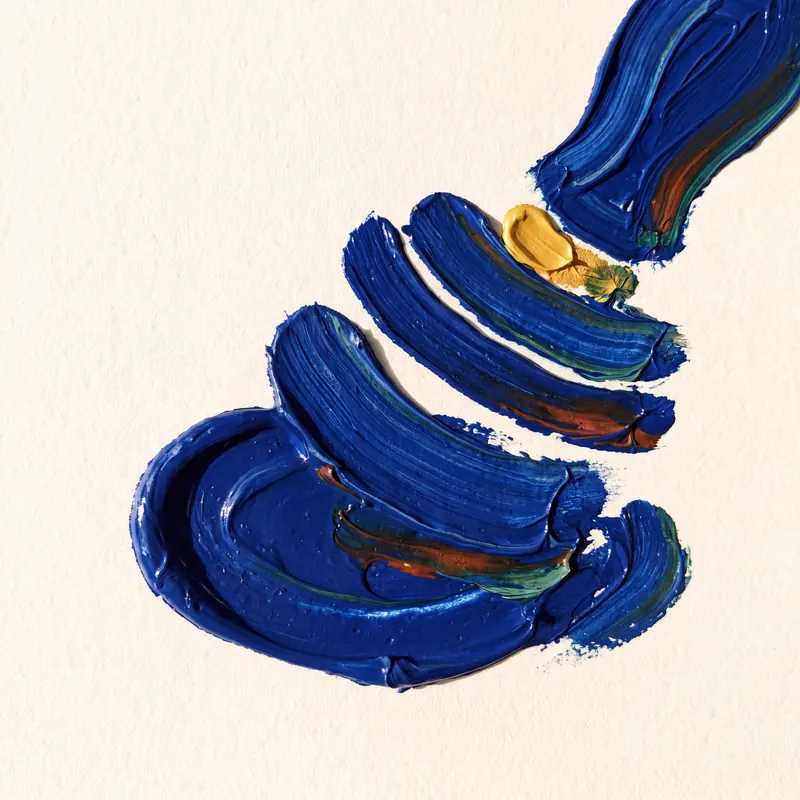 Thick ultramarine impasto strokes form a rosette with a single gold seal at its centre on cream handmade paper.