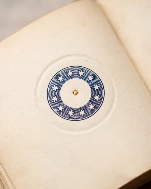 A circular blue emblem with twelve stars and a central gold rivet is impressed on the aged, cream-colored page of an antique book.