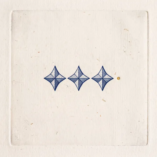 Three blue patterned diamond shapes arranged horizontally on textured cream paper within a debossed square frame, with a small gold dot to the right.